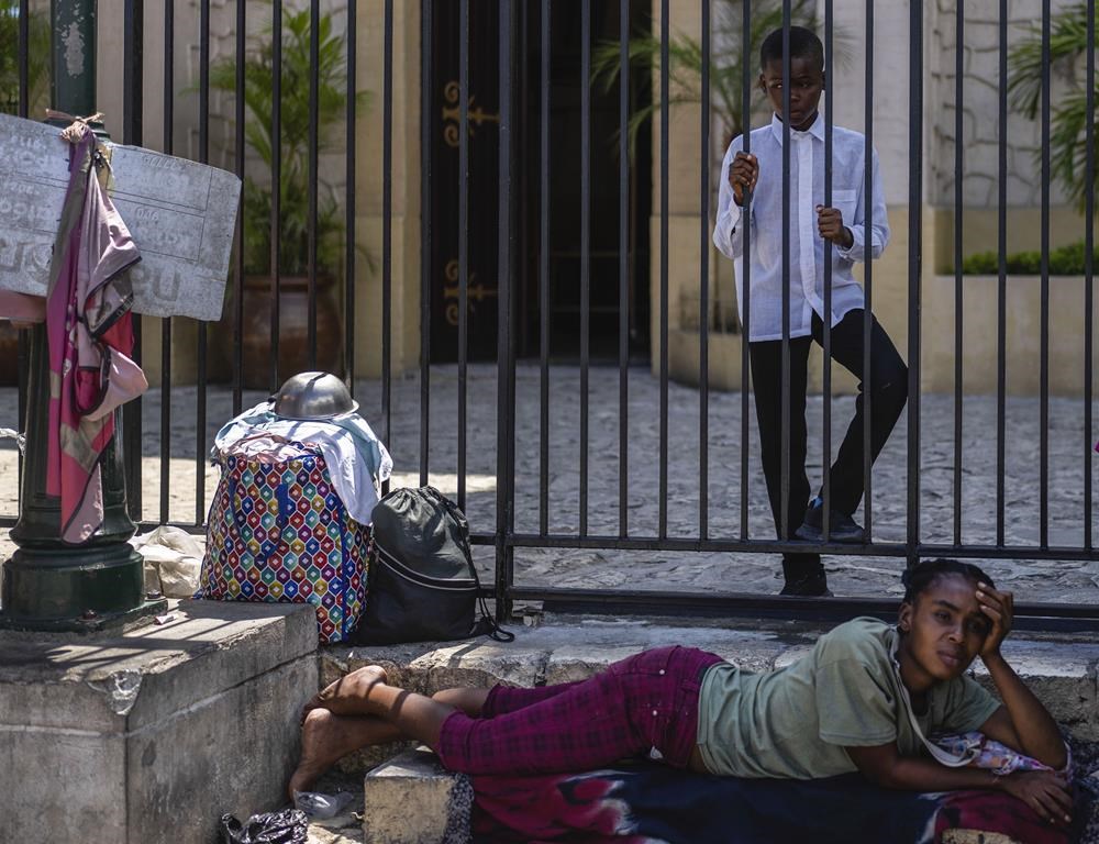 A youth stands beside a woman lying in front of a church in Port-au-Prince, Haiti, Sunday, April 28, 2024. (AP Photo/Ramon Espinosa)