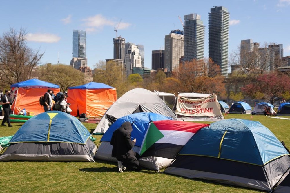 A protester attaches a Palestinian flag to a tent at an encampment set up on the University of Toronto campus on Thursday, May 2, 2024. THE CANADIAN PRESS/Chris Young