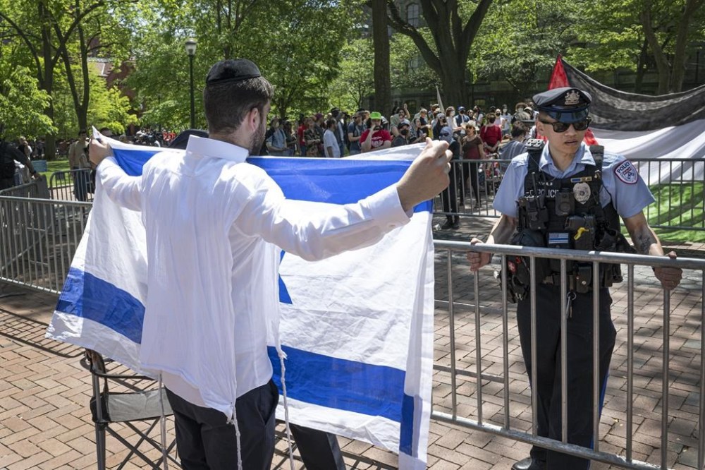 A pro-Israel supporter waves the Israeli flag in front of a police officer and a pro-Palestinian camp at the University of Pennsylvania encampment Thursday, May 2, 2024, in Philadelphia. (Jose F. Moreno/The Philadelphia Inquirer via AP)