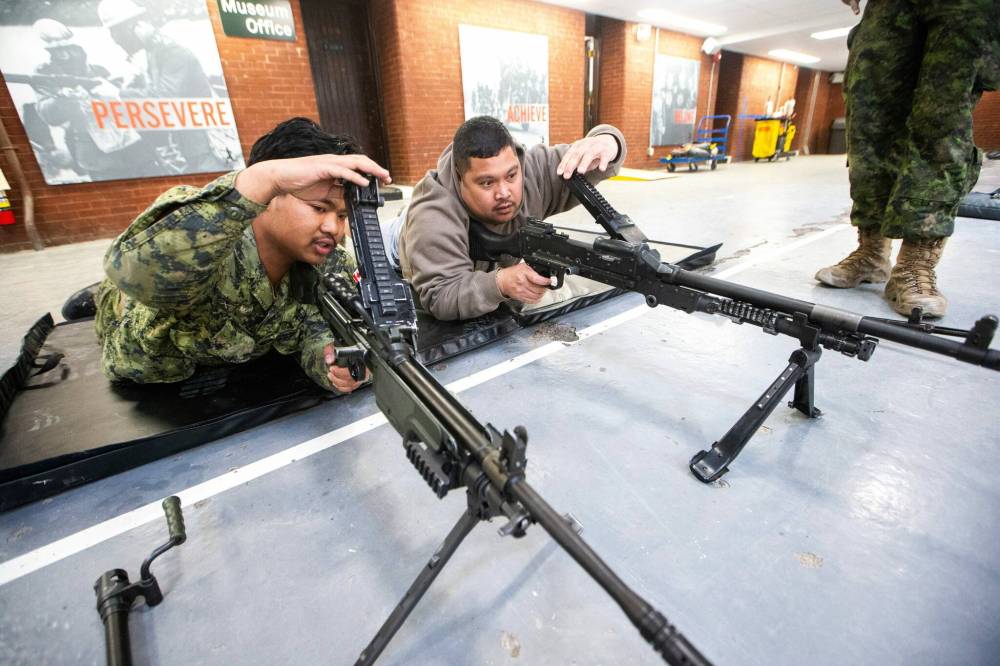 MIKAELA MACKENZIE / FREE PRESS Corporal Van Mang (left) demonstrates infanteer weaponry (C6 and C9 machine guns) to Mark Requinta during an open house, which is hoping to aid army recruitment efforts, at Minto Armouries.