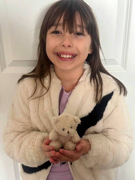 Nevaeh, 8, with a stuffed, white teddy bear given to her by RM of Taché firefighters after they freed her. (Supplied)
