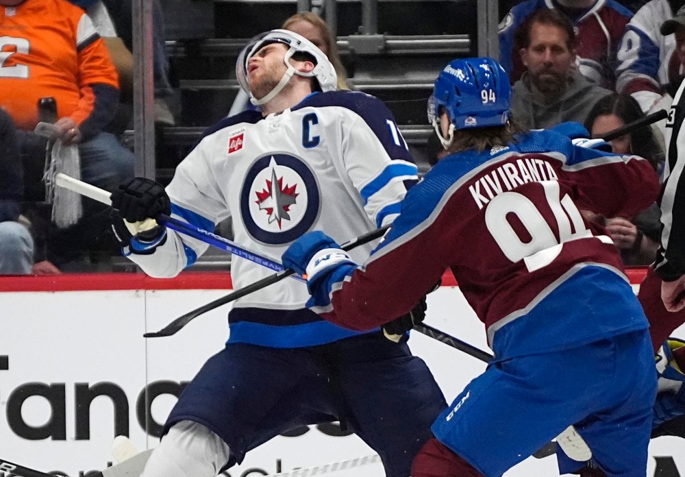 Adam Lowry (left) reels after being hit by winger Joel Kiviranta during the second period in Denver. (David Zalubowski / The Associated Press)