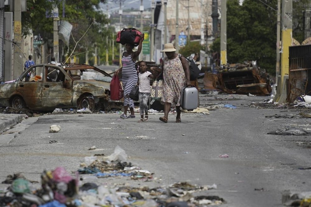 Residents walk past a burnt car blocking the street as they evacuate the Delmas 22 neighborhood to escape gang violence in Port-au-Prince, Haiti, Thursday, May 2, 2024. THE CANADIAN PRESS/AP-Ramon Espinosa