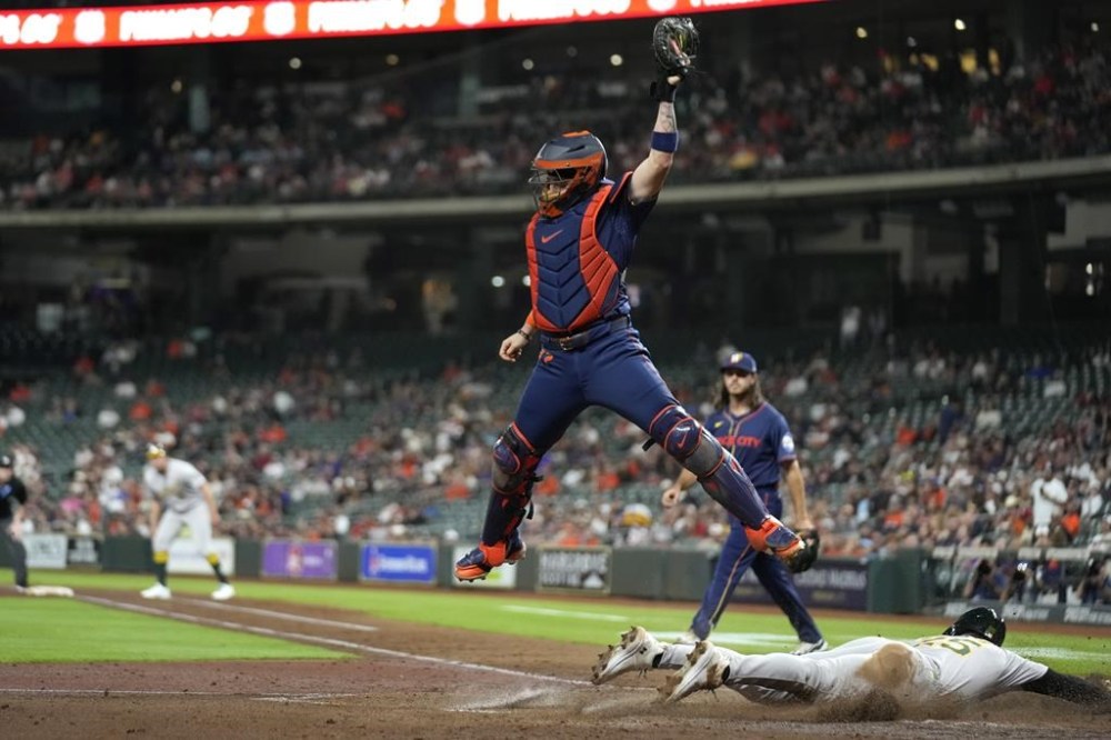 Oakland Athletics' Brent Rooker (25) slides under Houston Astros catcher Victor Caratini to score during the fourth inning of a baseball game Monday, May 13, 2024, in Houston. (AP Photo/David J. Phillip)