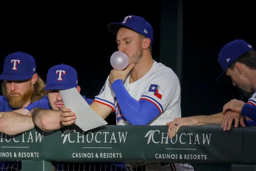 Texas Rangers' Andrew Knizner, center, blows a gum bubble in the dugout during the first inning of a baseball game against the Cleveland Guardians, Monday, May 13, 2024, in Arlington, Texas. (AP Photo/Gareth Patterson)