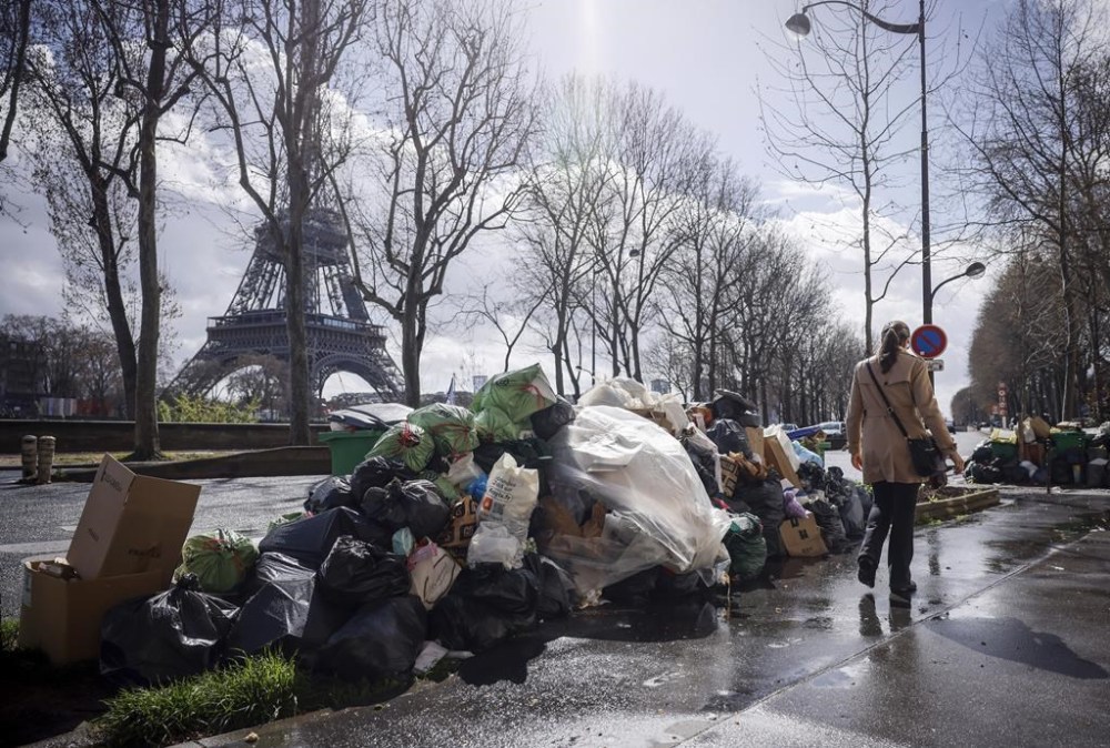 FILE - A woman walks past a pile of uncollected garbage near Eiffel Tower in Paris, Friday, March 24, 2023. Paris garbage collectors have lifted the strike notice that threatened to leave the French capital city under piles of junk during the Olympic Games after striking a deal that will improve their pay. Paris City Hall said in a statement on Wednesday, May 15, 2024 it sealed a deal with the workers and that the strike notice covering several days in May and a period from July to Sept. 8 had been lifted (AP Photo/Thomas Padilla, File)