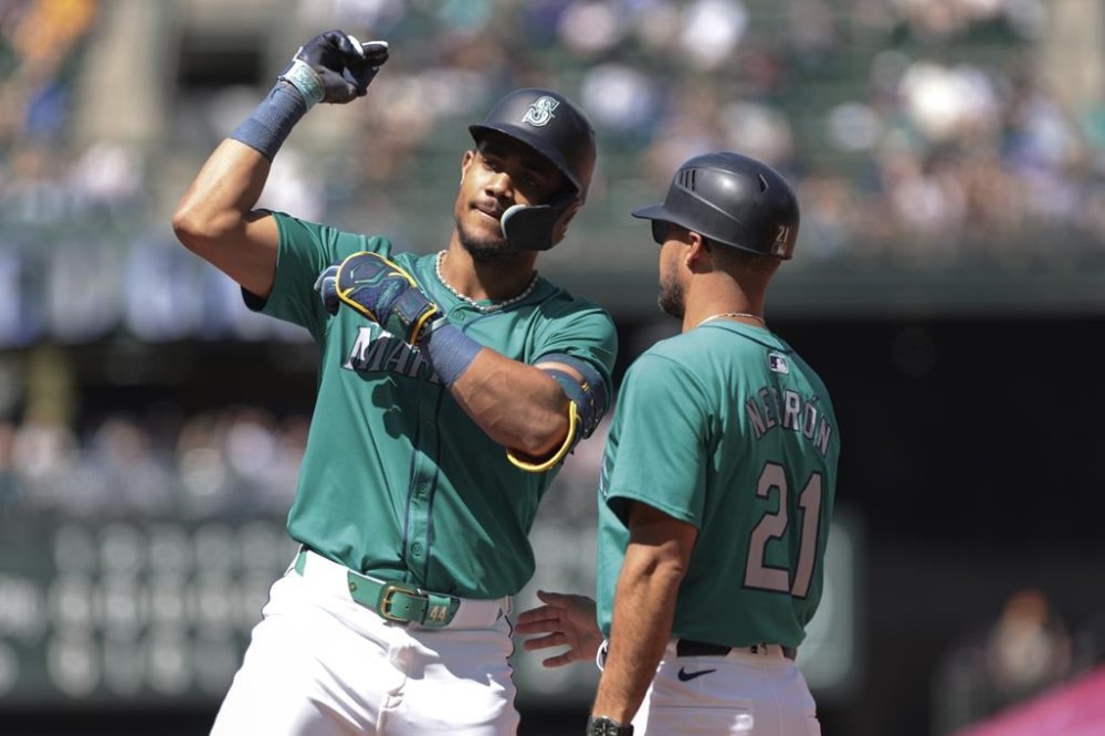 Seattle Mariners' Julio Rodríguez, left, celebrates with first base coach Kristopher Negron after hitting a single against the Kansas City Royals during the fifth inning of a baseball game Wednesday, May 15, 2024, in Seattle. (AP Photo/Jason Redmond)