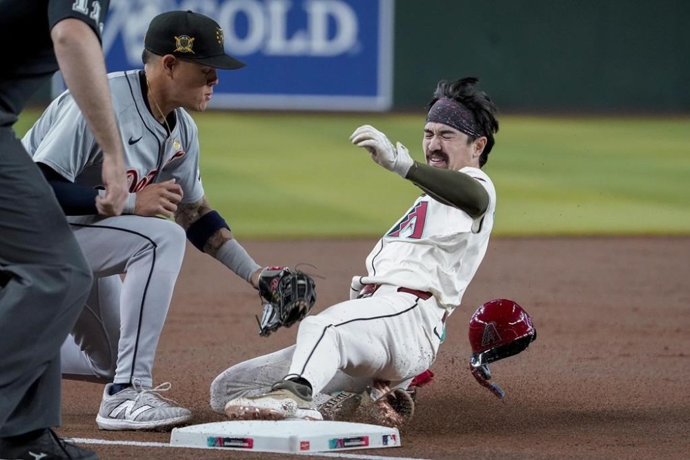 Arizona Diamondbacks' Corbin Carroll, right, slides into third base before a tag by Detroit Tigers third base Gio Urshela, second from right, during the first inning of a baseball game Sunday, May 19, 2024, in Phoenix. (AP Photo/Darryl Webb)