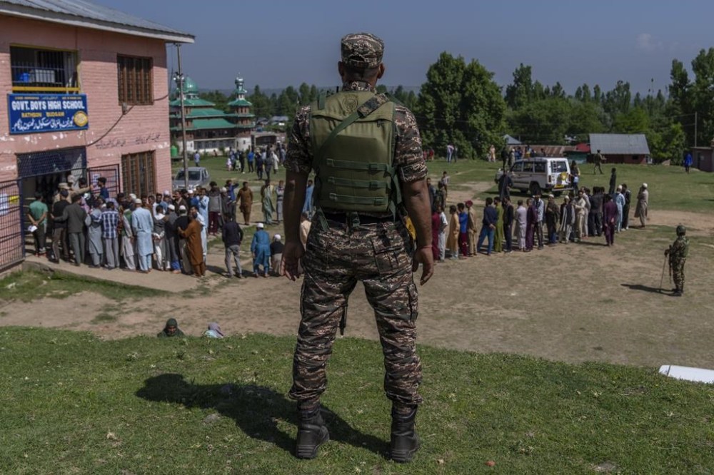 A paramilitary soldier stands guard near Kashmiri villagers who are queuing up to vote outside a polling booth during the fifth round of multi-phase national election in Rathson village west of Srinagar, Indian controlled Kashmir, Monday, May 20, 2024. (AP Photo/Dar Yasin)