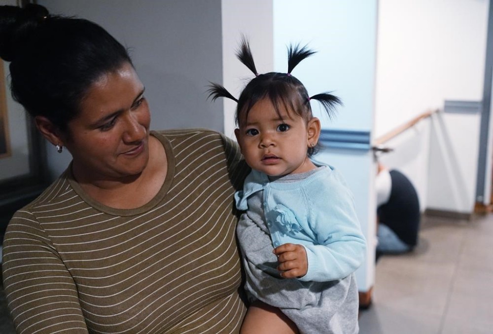 One-year-old Alexa is cradled by her mother as they wait to attend an orientation session for recent immigrants, Monday, May 20, 2024, in Denver. (AP Photo/David Zalubowski)