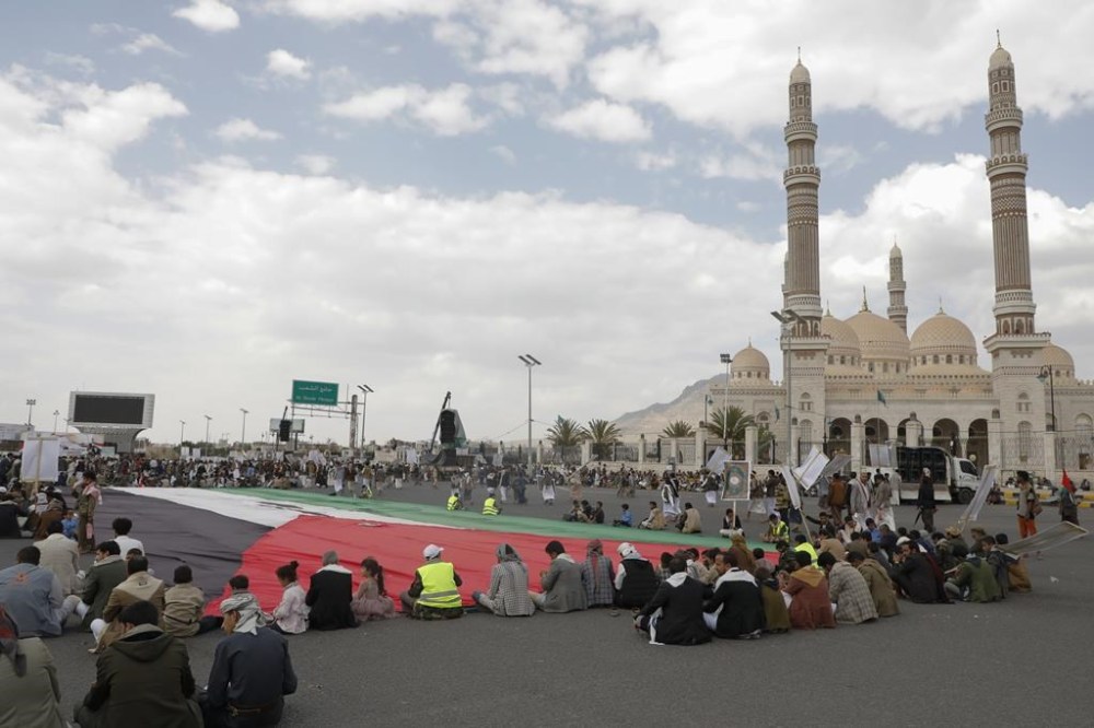 Houthi supporters sit in front of a giant Palestinian flag during a rally against the U.S.-led strikes against Yemen and in support of Palestinians in the Gaza Strip, in Sanaa, Yemen, Friday, May 17, 2024. (AP Photo/Osamah Abdulrahman)
