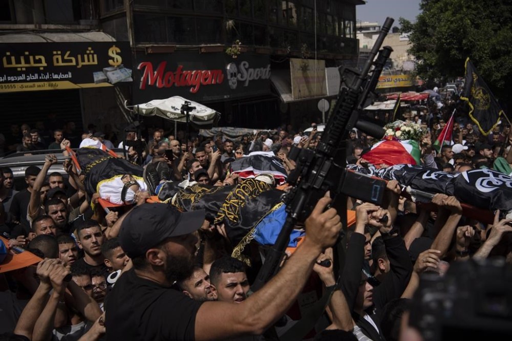 A gunman holds up his weapon as mourners carry the bodies of Palestinians, some draped in the Islamic Jihad militant group flags, during their funeral in the West Bank city of Jenin, Thursday, May 23, 2024. The Israeli military said Thursday it has completed a two-day operation in the occupied West Bank that the Palestinian Health Ministry says killed 12 Palestinians. Militant groups claimed at least eight of the dead as fighters, one from Hamas and seven from the Al-Aqsa Martyrs Brigade. (AP Photo/Leo Correa)