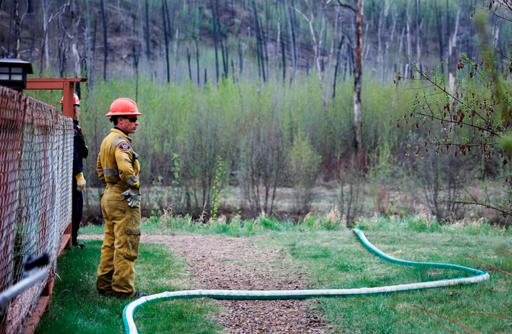 A firefighter monitors a wildfire sprinkler hose in the evacuated neighbourhood of Grayling Terrace in Fort McMurray, Alta., Thursday, May 16, 2024. Cool, wet weather over the past week has lowered the risk of wildfires in Alberta. THE CANADIAN PRESS/Jeff McIntosh