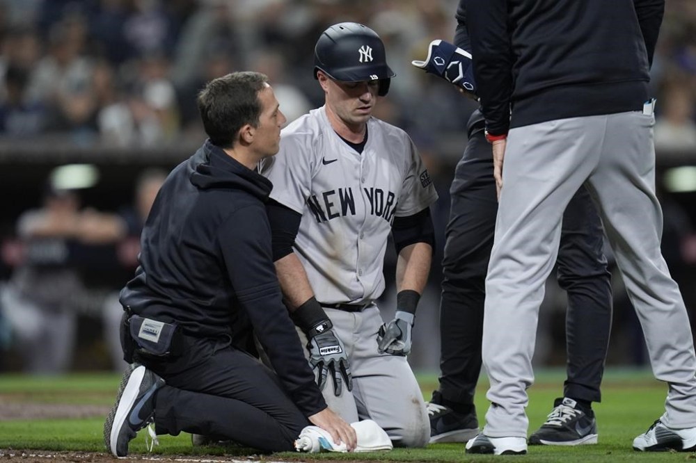 New York Yankees' Jon Berti, center, is helped by trainers after an injury while batting during the ninth inning of a baseball game against the San Diego Padres, Friday, May 24, 2024, in San Diego. (AP Photo/Gregory Bull)