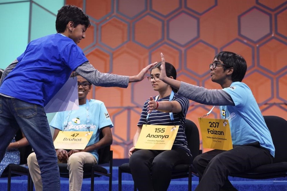Shrey Parikh, 12, of Rancho Cucamonga, Calif., left, high-fives Ananya Rao Prassanna, 13, of Apex, N.C., second from right, and Faizan Zaki, 12, of Allen, Texas, right, while competing during the finals of the Scripps National Spelling Bee, in Oxon Hill, Md., Thursday, May 30, 2024. (AP Photo/Nathan Howard)