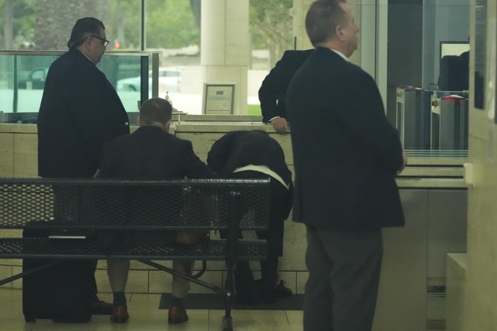 Ippei Mizuhara, center, the former longtime interpreter for the Los Angeles Dodgers baseball star Shohei Ohtani, removes his shoes to go through security at federal court, Tuesday, June 4, 2024, in Los Angeles. Mizuhara pleaded guilty to bank and tax fraud on Tuesday and admitted to stealing nearly $17 million from the Japanese baseball player to pay off sports betting debts. (AP Photo/Damian Dovarganes)