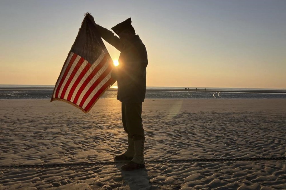 Christophe Receveur, of France, unfurls an American flag he bought six month ago in Gettysburg, Penn., to mark D-Day, Thursday, June 6, 2024 on Utah Beach, Normandy. As the sun sets on the D-Day generation, it's rising again over Normandy beaches where soldiers fought and died exactly 80 years ago, kicking off intense anniversary commemorations Thursday against the backdrop of renewed war in Europe, in Ukraine. (AP Photo/John Leicester)