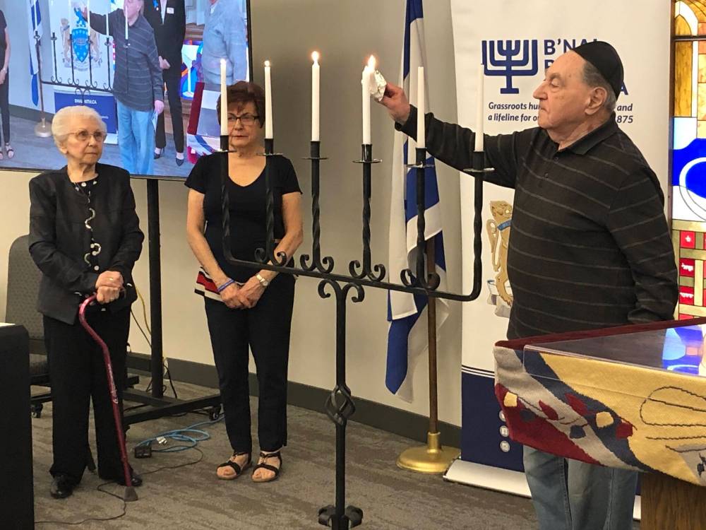 Edie Shuster (left) and Judy Lavitt look on as Aharon Berman lights a memorial candle Monday at the Unto Every Person There is a Name event to remember Holocaust victims. (John Longhurst / Free Press)