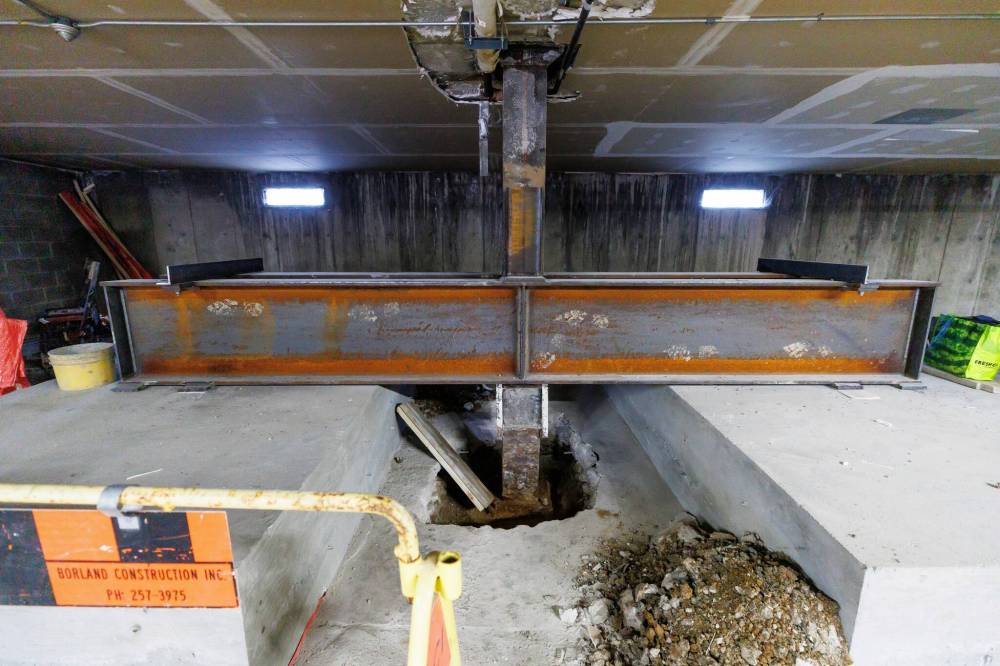 Workers stand by one of the massive metal beams that have been installed in the parking garage to try to stabilize the support pillars which have fallen into disrepair. (Mike Deal / Free Press)