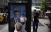 Commuters wait at a bus stop as an election poster depicting Greece's Kyriakos Mitsotakis reads 
