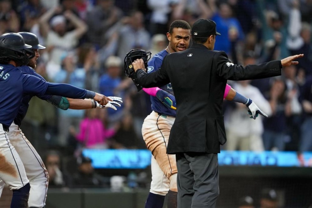 Seattle Mariners' Julio Rodríguez, back right, indicates to home plate umpire Gabe Morales he was safe sliding into home to score against the Chicago White Sox as teammates Josh Rojas, left front, and Luke Raley gesture during the seventh inning of a baseball game Tuesday, June 11, 2024, in Seattle. Rodríguez was safe. (AP Photo/Lindsey Wasson)