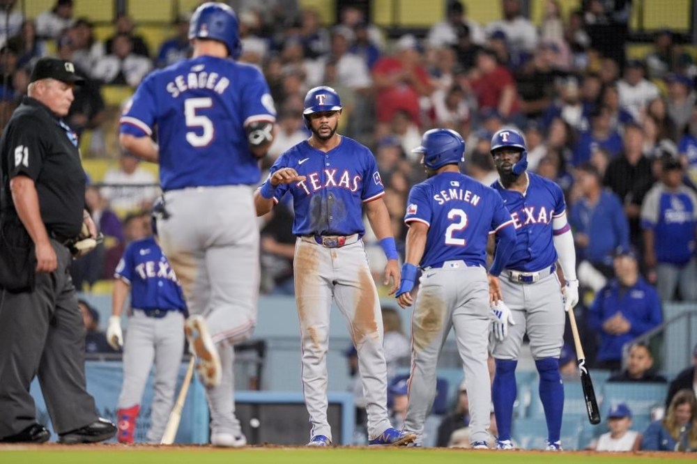 Texas Rangers designated hitter Corey Seager (5) scores on a three-run home run against the Los Angeles Dodgers as Leody Taveras, Marcus Semien and Adolis Garcia, from left, wait to congratulate him during the fifth inning of a baseball game Wednesday, June 12, 2024, in Los Angeles. (AP Photo/Ryan Sun)