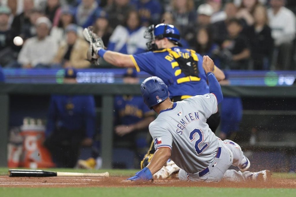 Texas Rangers' Marcus Semien (2) beats the throw to Seattle Mariners catcher Cal Raleigh, top, to score on a double by Nathaniel Lowe during the first inning of a baseball game, Friday, June 14, 2024, in Seattle. (AP Photo/Jason Redmond)