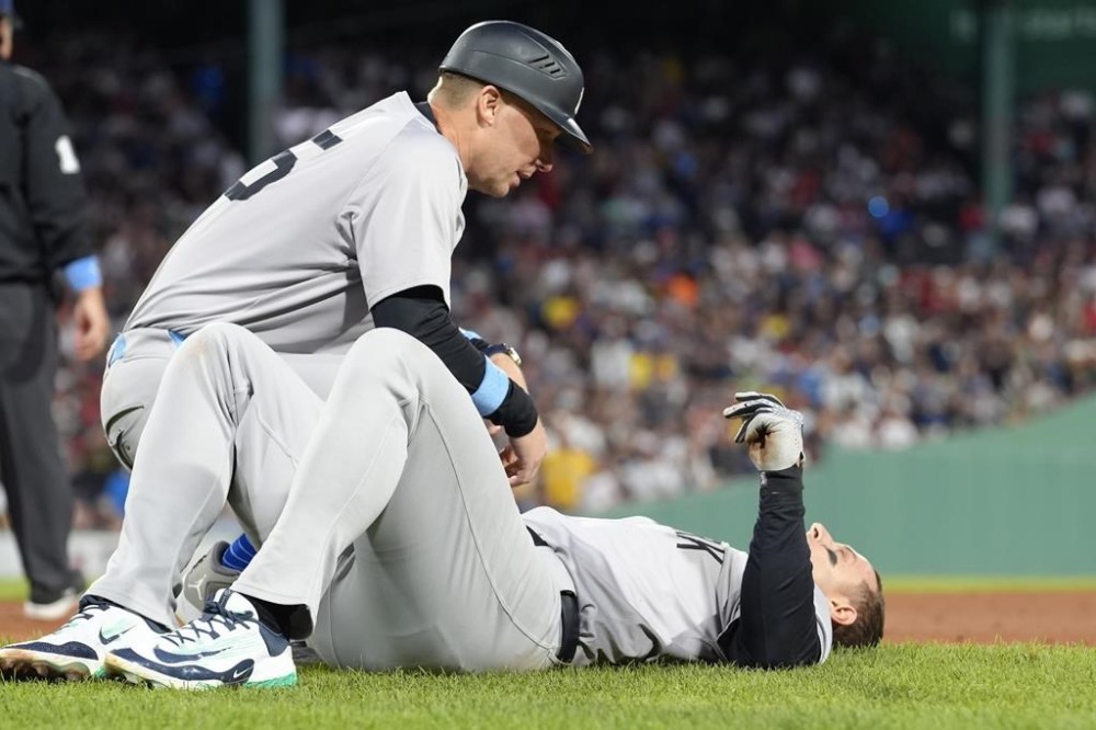 New York Yankees first base coach Travis Chapman, left, tends to Anthony Rizzo, right, following a first base collision in the seventh inning of a baseball game against the Boston Red Sox, Sunday, June 16, 2024, in Boston. Rizzo left the game after colliding with Red Sox pitcher Brennan Bernardino on a play at first and falling hard on his right wrist. (AP Photo/Steven Senne)