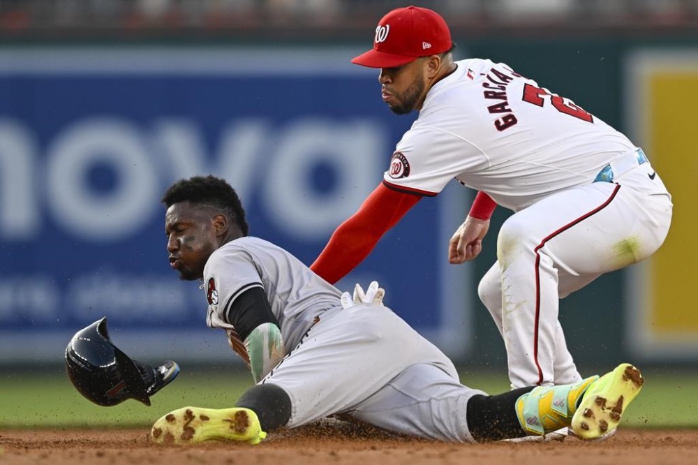 Arizona Diamondbacks' Geraldo Perdomo, left, beats the tag of Washington Nationals second baseman Luis Garcia Jr. for a double during the fifth inning of a baseball game Tuesday, June 18, 2024, in Washington. (AP Photo/John McDonnell)