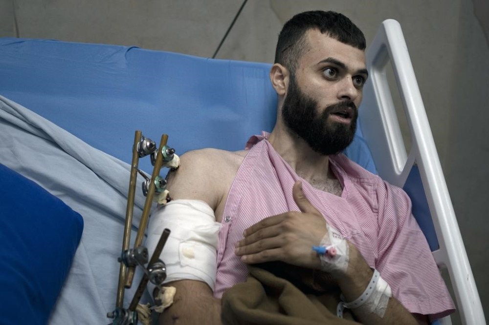 Mujahid Abadi, 24, recounts his experience of being thrown by Israeli soldiers onto the hood of their military jeep, bleeding from his arm and leg after soldiers shot him, as he recovers at the Ibn Sina Specialized Hospital in the West Bank city of Jenin, Tuesday, June 25, 2024. When the Palestinian man stepped outside to see if Israeli forces had entered his uncle's neighborhood, he was shot in the arm and the foot. That was only the start of his ordeal. Hours later, beaten and bloodied, he found himself strapped to the searing hood of an Israeli military jeep driving down a road. (AP Photo/Maya Alleruzzo)