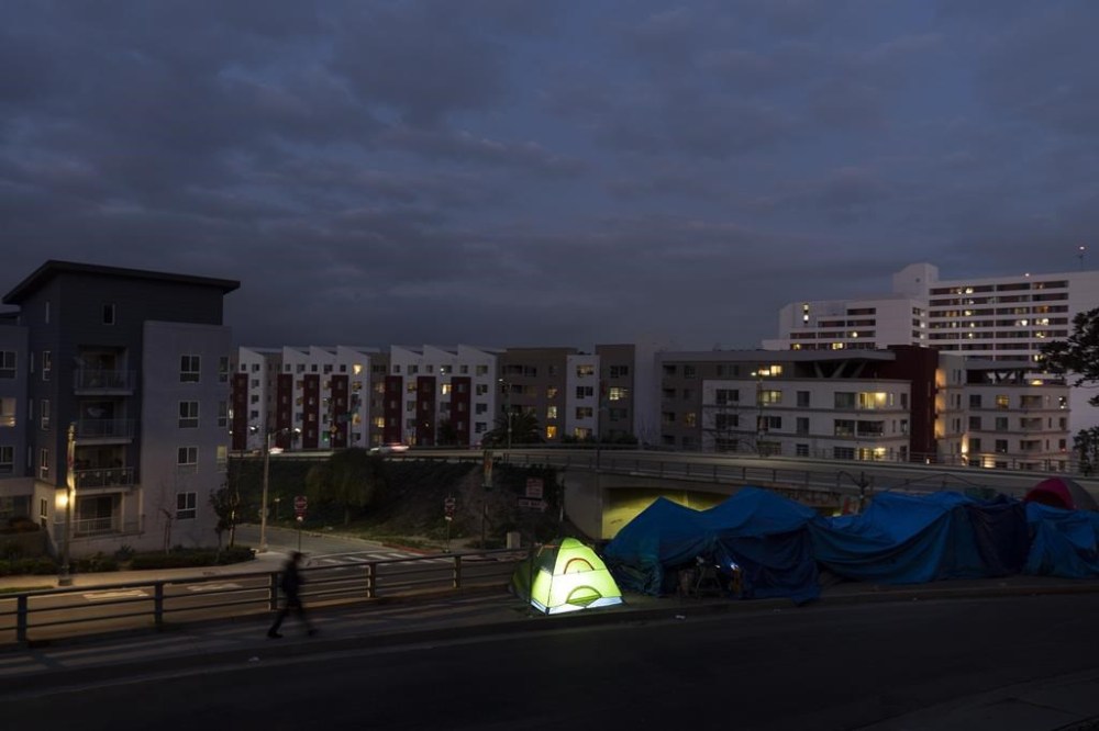 FILE - In this photo illuminated by an off-camera flash, a man walks past a small homeless encampment near Chinatown in Los Angeles, Feb. 13, 2023. The Supreme Court ruled on Friday, June 28, 2024, that cities can enforce bans on homeless people sleeping outdoors in West Coast areas where shelter space is lacking. (AP Photo/Jae C. Hong, File)