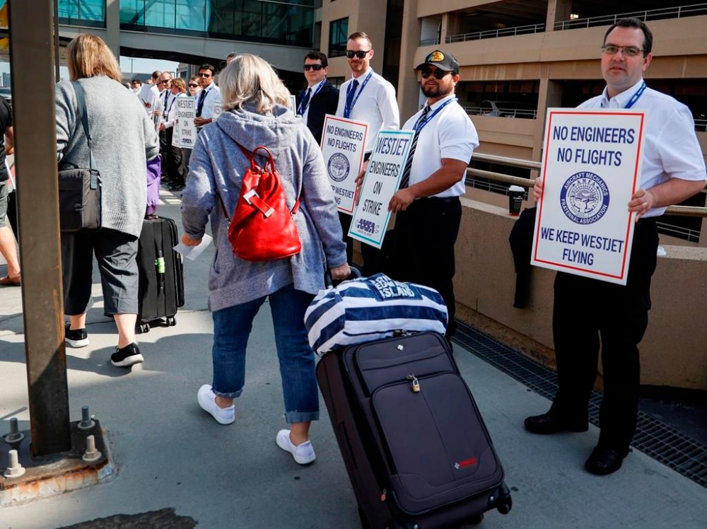 WestJet says there will still be flight disruptions, including cancellations, this week after a deal was reached to end a strike by its mechanics. Passengers make their way past striking WestJet mechanics at Calgary International Airport in Calgary, Saturday, June 29, 2024. THE CANADIAN PRESS/Jeff McIntosh