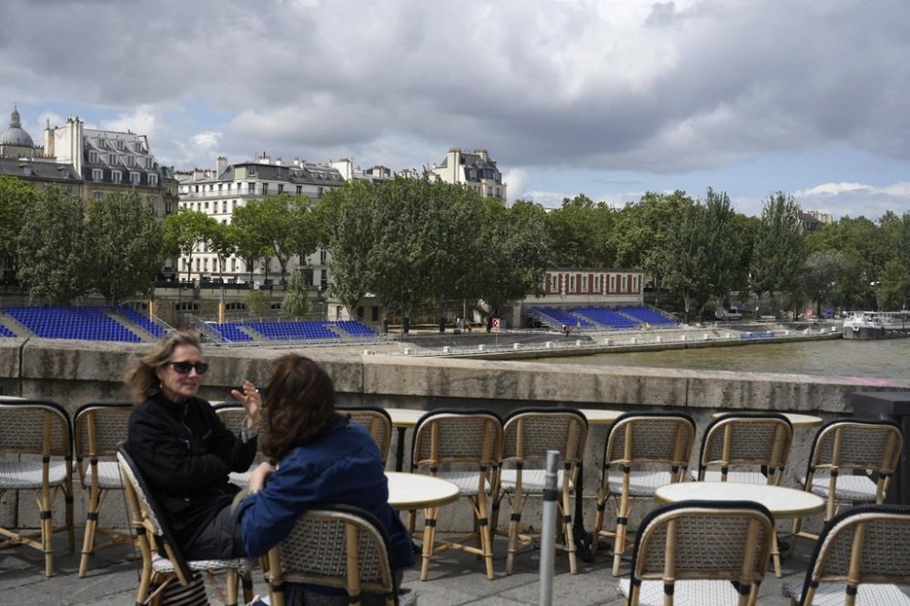 Women discuss by the Seine river with stands installed on its banks, Thursday, July 4, 2024 in Paris. The Seine river will host the Paris Olympic Games opening ceremony on July 26. (AP Photo/Thibault Camus)