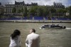 People sit along the Seine river with stands installed on its banks, Thursday, July 4, 2024 in Paris. The Seine river will host the Paris Olympic Games opening ceremony on July 26. (AP Photo/Thibault Camus)