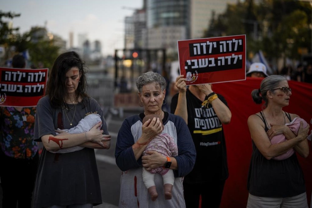 Relatives and supporters of Israeli hostages held by Hamas in the Gaza Strip hold baby dolls during a performance marking nine months since the start of the war and calling for their return, in Tel Aviv, Israel, Sunday, July 7, 2024. (AP Photo/Leo Correa)