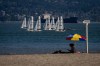 A person sits on the beach under a colourful umbrella as sailboats pass in Vancouver, B.C., Sunday, July 7, 2024. Heat warnings have been put in place for the Metro Vancouver area for elevated temperatures. THE CANADIAN PRESS/Ethan Cairns