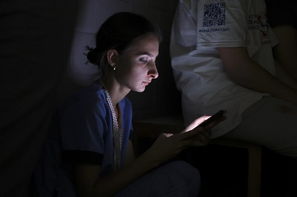 A nurse looks at her phone as she takes shelter in a basement after Russian missile hit the country's main children hospital Okhmadit in Kyiv, Ukraine, Monday, July 8, 2024. The daytime barrage targeted five Ukrainian cities with more than 40 missiles of different types hitting apartment buildings and public infrastructure, President Volodymyr Zelenskyy said on social media. (AP Photo/Anton Shtuka)