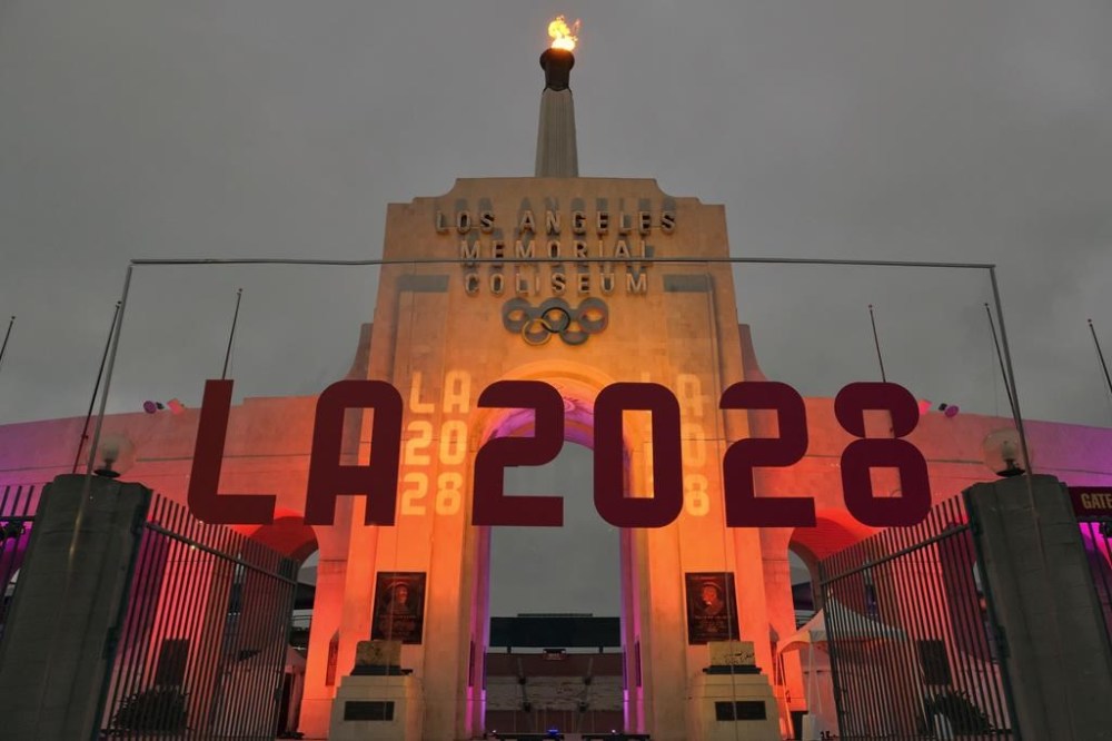 FILE - An LA 2028 sign is seen in front of the Olympic cauldron at the Los Angeles Memorial Coliseum, Wednesday, Sept. 13, 2017. The 2028 Los Angeles Olympics have announced more venue assignments, with the cities of Carson and Long Beach reprising their roles from previous games held in the region. (AP Photo/Richard Vogel, File)