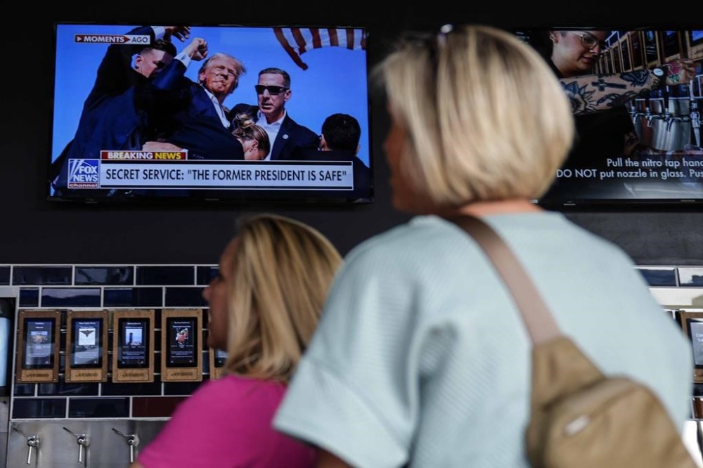 People watch news near the Fiserv Forum ahead of the 2024 Republican National Convention, Saturday, July 13, 2024, in Milwaukee. Former president Donald Trump was whisked off the stage at a rally in Butler, Pennsylvania after apparent gunshots rang through the crowd.(AP Photo/Matt Rourke)