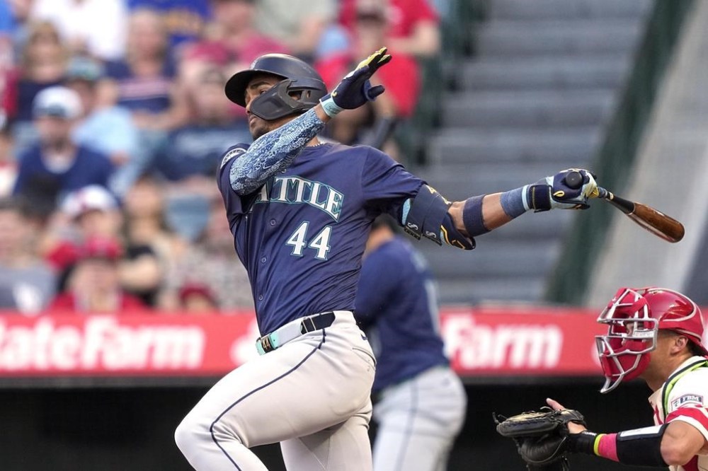 Seattle Mariners' Julio Rodriguez, left, hits an RBI single as Los Angeles Angels catcher Logan O'Hoppe watches during the first inning of a baseball game Saturday, July 13, 2024, in Anaheim, Calif. (AP Photo/Mark J. Terrill)