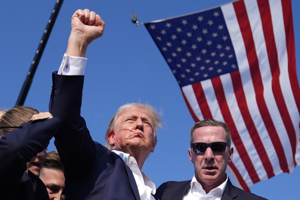 Republican presidential candidate former President Donald Trump reacts as he is surrounded by U.S. Secret Service agents at a campaign rally, Saturday, July 13, 2024, in Butler, Pa. The image of Trump pumping his fist into the air with an American flag in the background, as blood trickles down the side of the former president’s face, came at a critical time in an increasingly polarized political climate for the United States. THE CANADIAN PRESS/AP/Evan Vucci