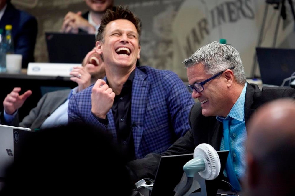 Seattle Mariners Executive Vice President & General Manager Justin Hollander, far left, President, Baseball Operations Jerry Dipoto, second from left, react after Senior Director, Amateur Scouting Scott Hunter, right, makes the selection for the team's first pick of Jurrangelo Cijntje, of Mississippi State, in the draft room at T-Mobile Park during the MLB baseball draft, Sunday, July 14, 2024, in Seattle. (AP Photo/John Froschauer)