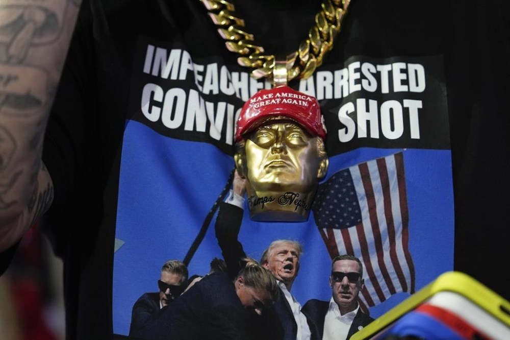 A delegate wears a tee shirt with a photo of Republican presidential candidate former President Donald Trump being surrounded by U.S. Secret Service agents at a campaign rally during the Republican National Convention Monday, July 15, 2024, in Milwaukee. (AP Photo/Julia Nikhinson)