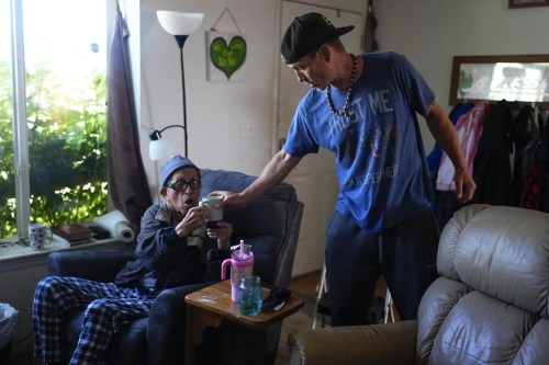 FILE - Sonny Curley hands a cup of coffee to his father Harold Curley at their home near the ocean Wednesday, May 22, 2024, on the Quinault reservation in Taholah, Wash. The home has a rotting deck and black mold inside, and the family has had to evacuate several times due to flooding. (AP Photo/Lindsey Wasson, File)