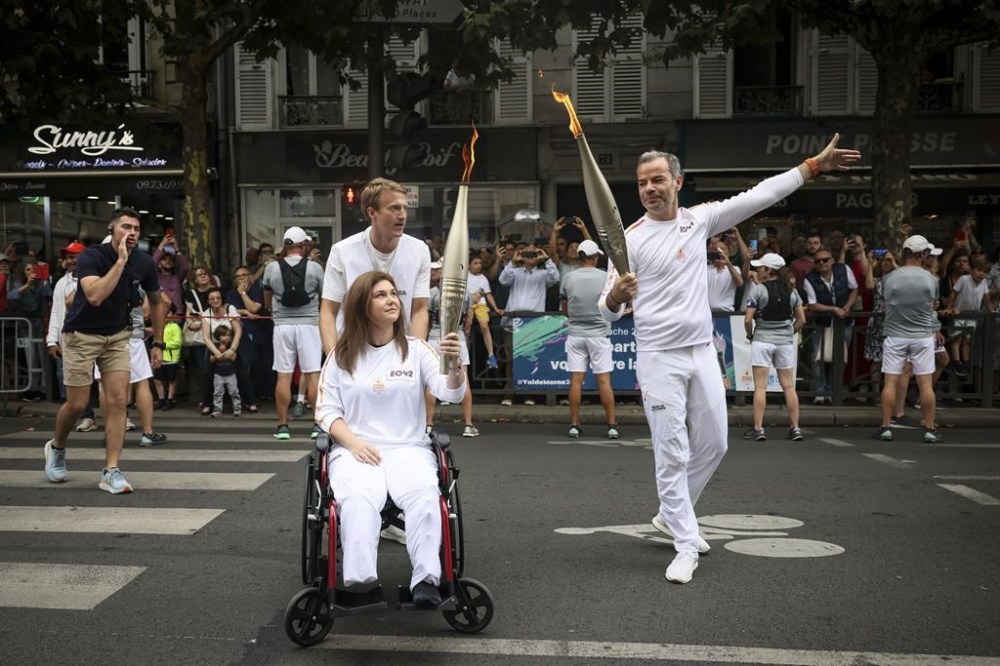 Press agency photographer Christina Assi, left, holds the Olympic torch with. Tinam Pung, right, at the 2024 Summer Olympics, Sunday, July 21, 2024, in Vincennes, outside Paris, France. Assi was struck by a tank shell on Oct. 13, 2023 while reporting clashes between the Israeli army and armed groups in southern Lebanon. (AP Photo/Thomas Padilla)