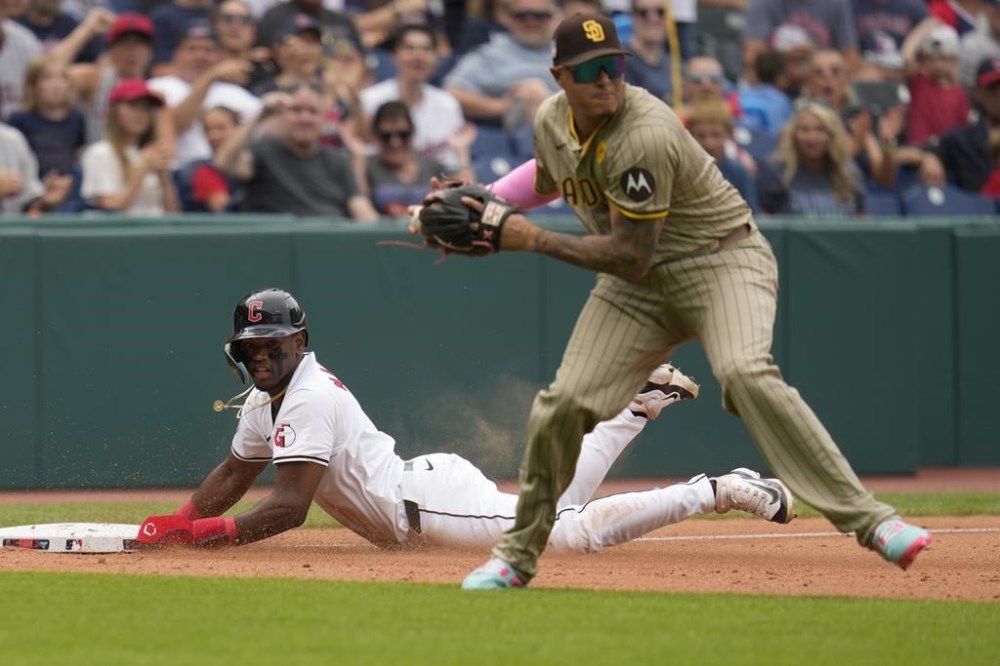 Cleveland Guardians' Angel Martínez, left, slides safely into third base as San Diego Padres third baseman Manny Machado, right, throws to second base for an out against Guardians' José Ramírez in the seventh inning of a baseball game Sunday, July 21, 2024, in Cleveland. (AP Photo/Sue Ogrocki)