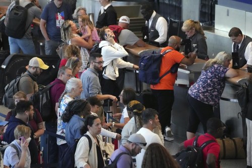 A traveller looks up while talking on a cellphone as passengers wait in line for assistance at the Delta Terminal, Friday, July 19, 2024, at Logan International Airport in Boston. (AP Photo/Michael Dwyer)