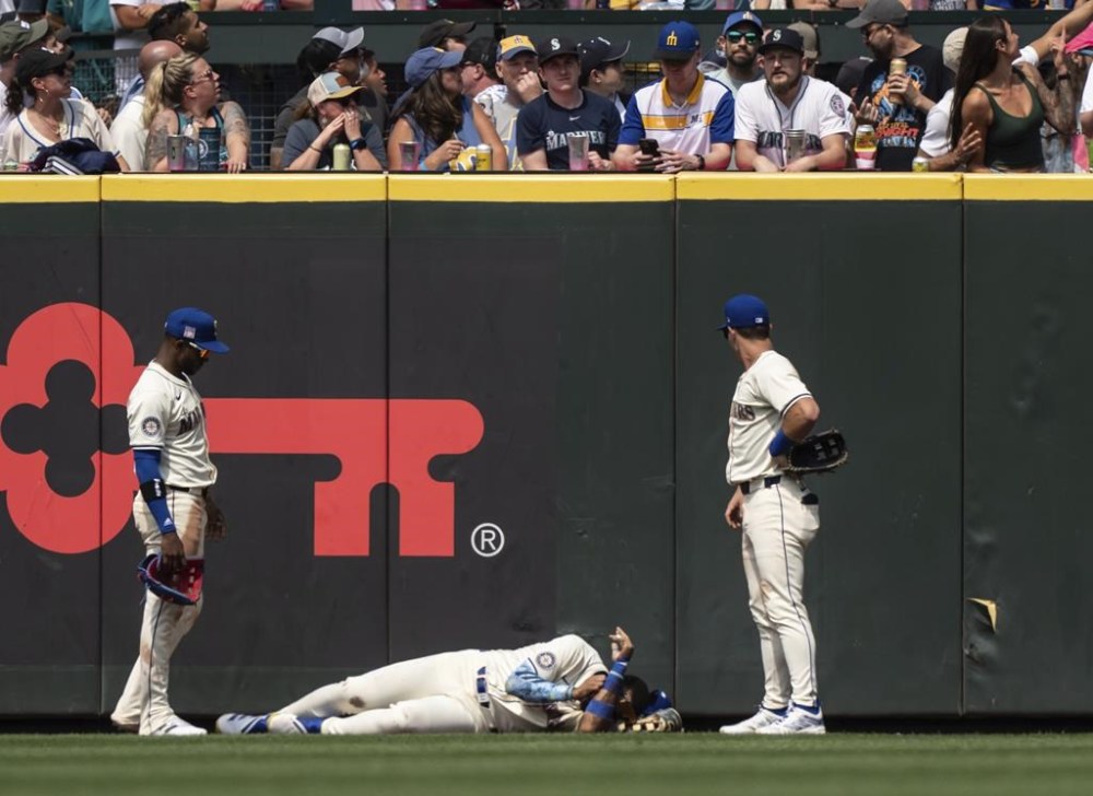 Seattle Mariners Julio Rodriguez, center, lies on the ground between right fielder Victor Robles, left, and left fielder Dylan Moore after crashing into the outfield wall during the eighth inning of a baseball game against the Houston Astros, Sunday, July 21, 2024, in Seattle. (AP Photo/Stephen Brashear)