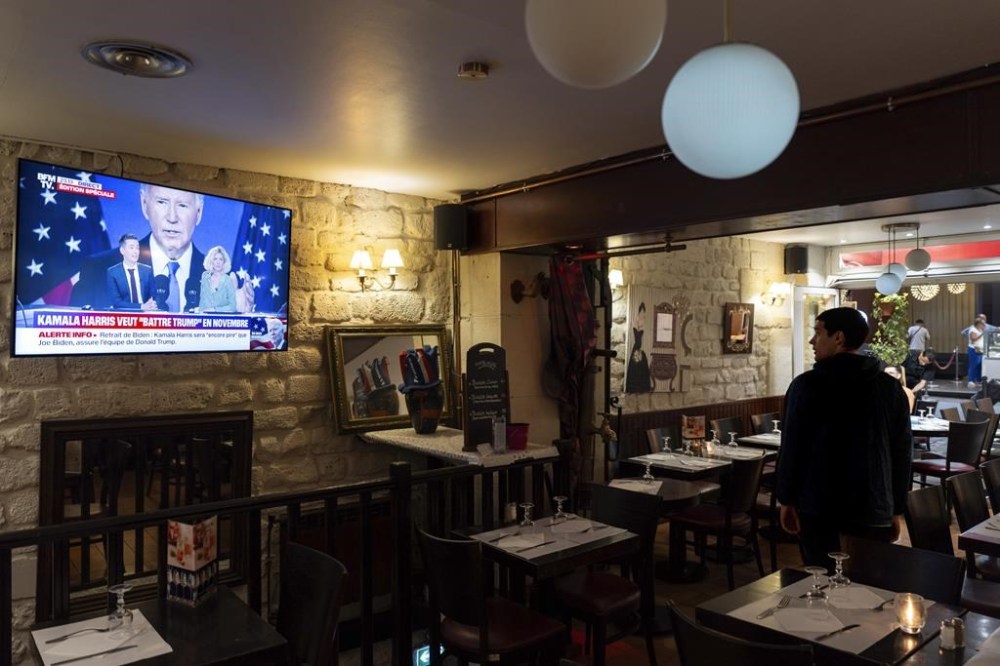 Mattia Crovino, of Bologna, Italy, watches a news broadcast announcing that President Joe Biden has dropped out of the 2024 race for the White House, Sunday, July 21, 2024,. (AP Photo/David Goldman)