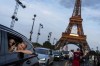 FILE - Passengers in the back of a taxi film themselves as they leave the Eiffel Tower decorated with the Olympic rings ahead of the 2024 Summer Olympics, Wednesday, July 17, 2024, in Paris. The city itself will be one of the protagonists of the 2024 Olympics. That's why the Eiffel Tower and Seine River are featured just as prominently as Simone Biles or Katie Ledecky in NBC’s ads. (AP Photo/David Goldman, File)